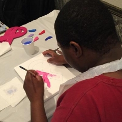 A participant is painting a pink ribbon.