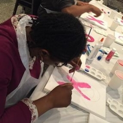 A participant is painting a pink ribbon.