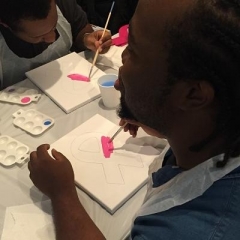 A participant is painting a pink ribbon.