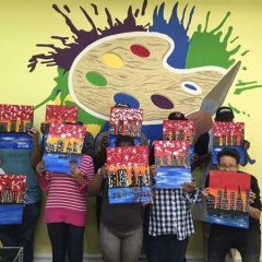 Participants holding up their completed paintings of the New York skyline.
