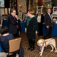 Andy Fisher is chatting with Holly Bonner, the creator of BlindMotherhood.com.  ID: Holly's  guide dog, Frances, is standing by her side.