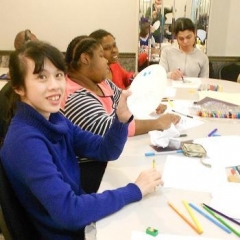Participants making art pieces for the art contest submission.  ID: A participant wearing dark blue is at the front.