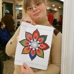 A participant holding up her artwork.  ID: An intricate drawing of a flower.