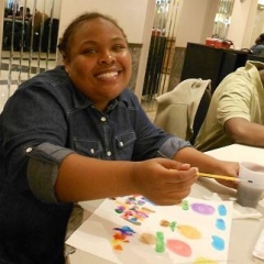 A participant working on her art project.  ID: A smiling participant holds a pencil over a drawing.