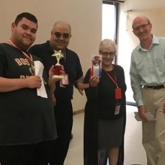 A participant posing with Brooklyn DDC representatives.  ID: A participant holding up a star shaped award.