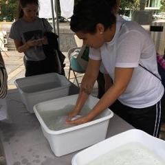 Participants wash white linens.  ID: A participant is leaning over a bucket of water.