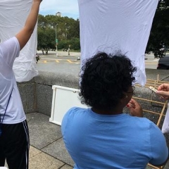 Participants hanging linens to dry.  ID: A participant is using clothes pins.