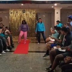 A participant is medeling her outfit.  ID: A girl walks down a red carpet.  She is wearing pink pants and a purple sweatshirt.