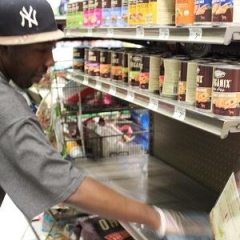 A participant is cleaning Petco product shelves.  ID: A participant is wearing a gray shirt, a black baseball cap, and rubber gloves.