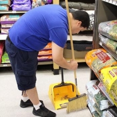 A participant is sweeping a floor at Petco.  ID: A participant wearing a blue shirt is bending down to sweep up the floor.