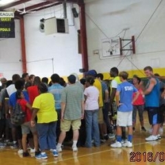 A group of participants are looking up at a score board.  ID: Participants assembled on a basketball court.