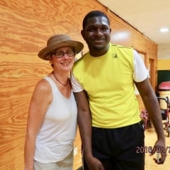 A participant and a board member pose for a picture.  ID: The board member is wearing a white shirt and a hat.  The participant is wearing a bright yellow shirt.