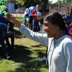 A participant holding up a toy.  ID: A participant  is wearing a gray t-shirt.