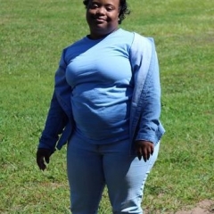 A participant smiling for the camera.  ID: A participant wearing a blue shirt is standing in the middle of grass.