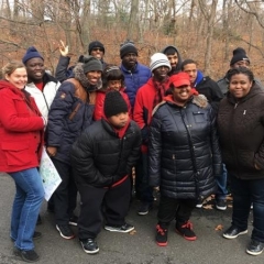 A group of participants pose for the camera before visitng the Bronx Zoo.  ID: Participants huddle together outdoors and smile for the picture.