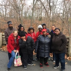 A group of participants pose for the camera before visitng the Bronx Zoo.  ID: Participants huddle together outdoors and smile for the picture.