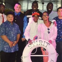 A group of participants smile for a group picture.  ID: Participants stand on board of a cruise in front of a life saver that reads "Spirit New Jersey 2017".