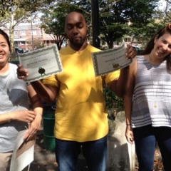 Day Habilitation participant holds up an award he received for participating in Therapeutic Garden Project for People of All Abilities.  ID: The participant is wearing a yellow shirt.