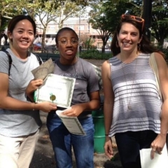 Day Habilitation participant holds up an award she received for participating in Therapeutic Garden Project for People of All Abilities.  ID: The participant stands in Dyker Beach Park posing for the camera.