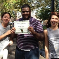 Day Habilitation participant holds up an award he received for participating in Therapeutic Garden Project for People of All Abilities.  ID: The participant is wearing a purple and white striped shirt.