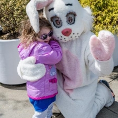 A girl is hugging Easter Bunny.  ID: A white Easter Bunny is hugging a little girl wearing a pink jacket.