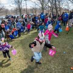 Kids run to hunt for Easter Eggs.  ID: Front center - A girl wearing a bunny mask is holding a pink basket.