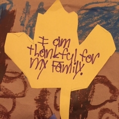 A yellow paper leaf handwritten by City Access participant as part of a larger mural.  ID: The leaf reads:  I am thankful for my family."