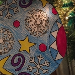 A colorful paper ornament made by City Access participants.  ID: Ornament with a yellow stars and white snowflakes.