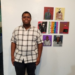 A participant poses next to a display of self portraits.