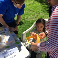 A little girl is making a headband at the arts  & crafts table.