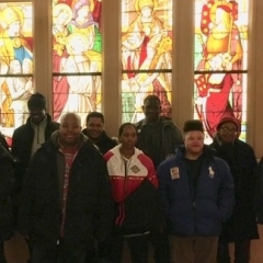 Participants pose for the camera.  ID: Standing in front stained glass windows.