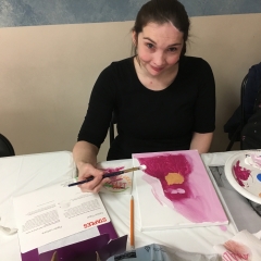 Participant smiles for the camera.  ID: She is holding a blush and is painting a self portrait.