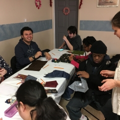 Participants working with various materials during an art class. ID: Sitting around a table with art supplies.