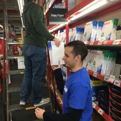One participant passes printing paper to another participant on a ladder to restock higher shelves.
