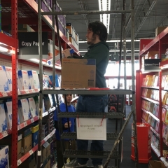 Participant stands on a ladder while restocking printing paper.